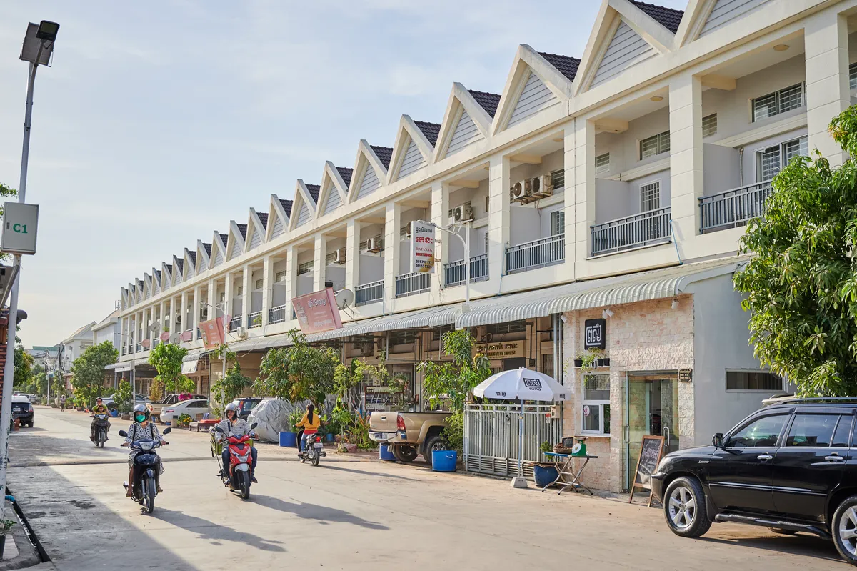 Occupied street of white gable-roofed Borey Maha Sen Sok houses with daily street life