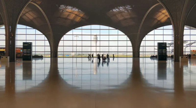 Interior of Techo International Airport's departure hall, with vaulted timber-lattice arches framing tall windows and the control tower beyond