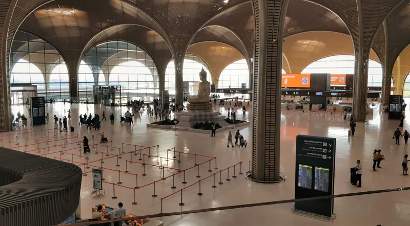 Concourse of Techo International Airport with passengers, soaring arched columns and a tall Buddha statue at its centre
