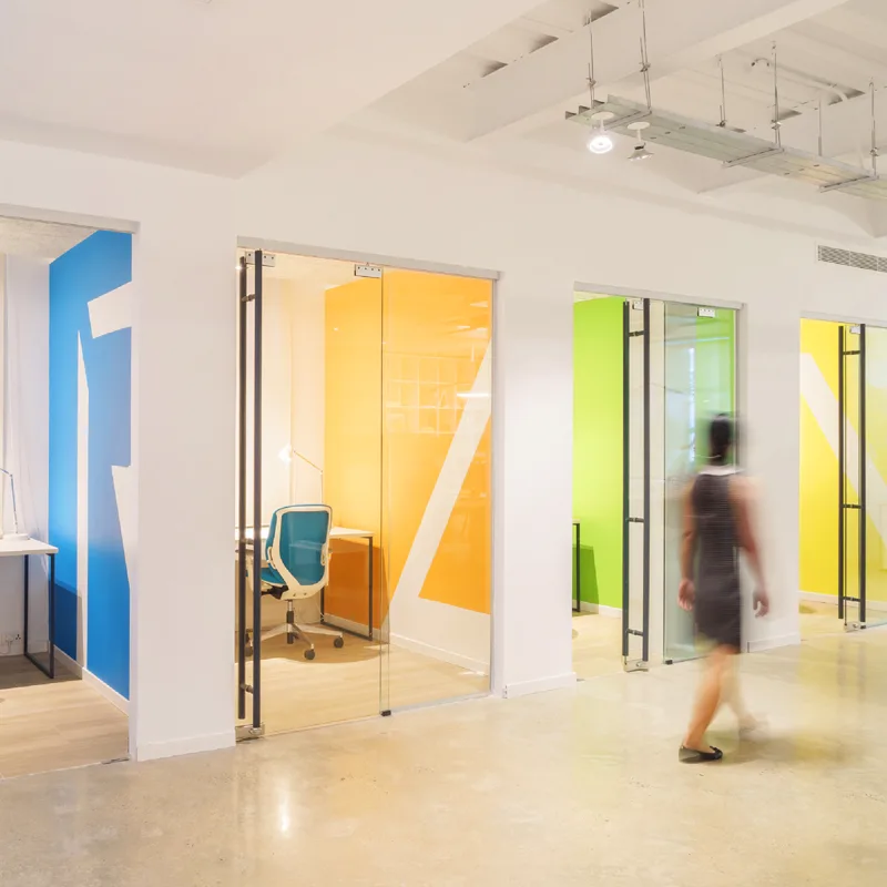 Raintree coworking corridor lined with glass-walled focus pods in blue, orange, green and yellow